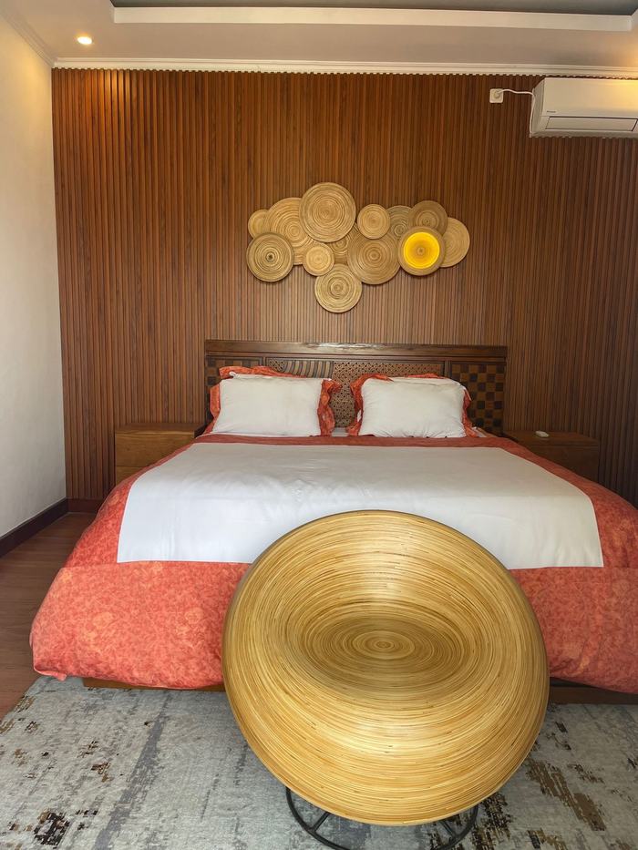 Primary bedroom in daylight with coral duvet and woven accent stool